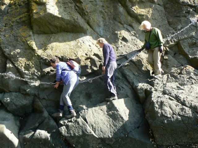 Three walkers using the fixed chains to cross steep rock on the Elie Chain Walk