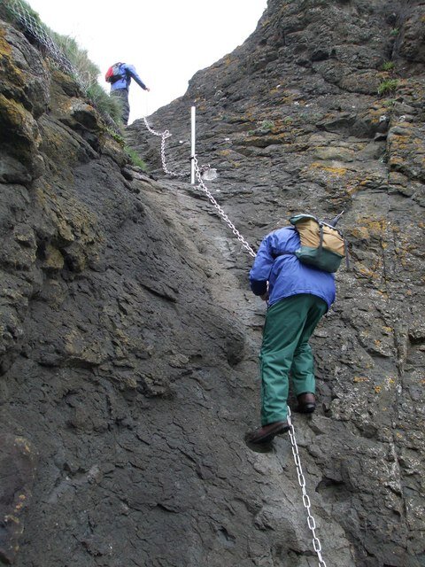 A walker climbing a near-vertical section of the Elie Chain Walk on a fixed chain