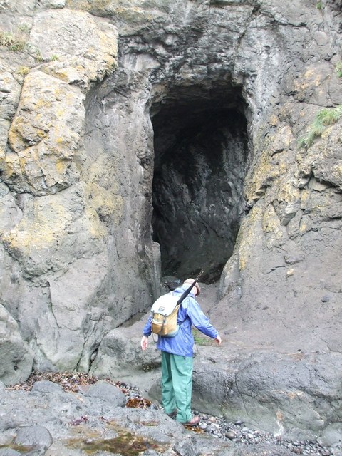 A walker standing at the tall entrance of the Doo Cave in the Kincraig cliffs