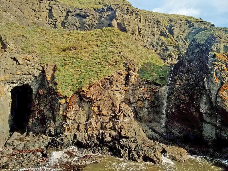 A cave mouth, a horizontal traverse chain and a near-vertical chain up a gully at Kincraig Point, with waves breaking below