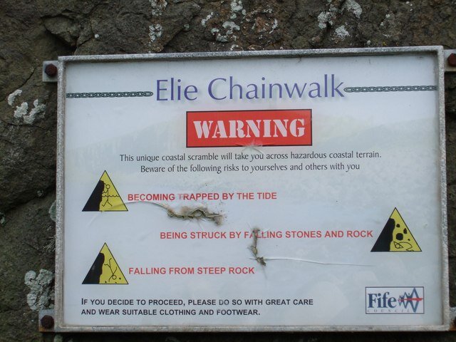 Official Fife Council warning sign at the entrance to the Elie Chainwalk listing the risks: becoming trapped by the tide, falling rocks, and falling from steep rock
