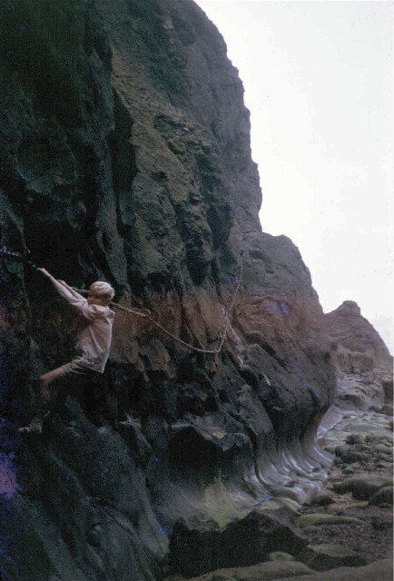 Black-and-white 1963 photograph of a person scrambling on a chain into Macduff's Cave
