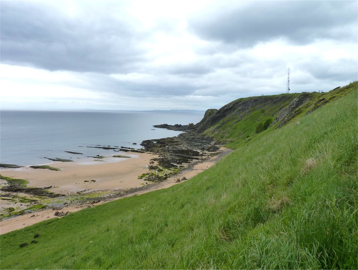 Grassy slope of Kincraig Hill above the rocky shore and Earlsferry beach, looking towards the start of the Chain Walk