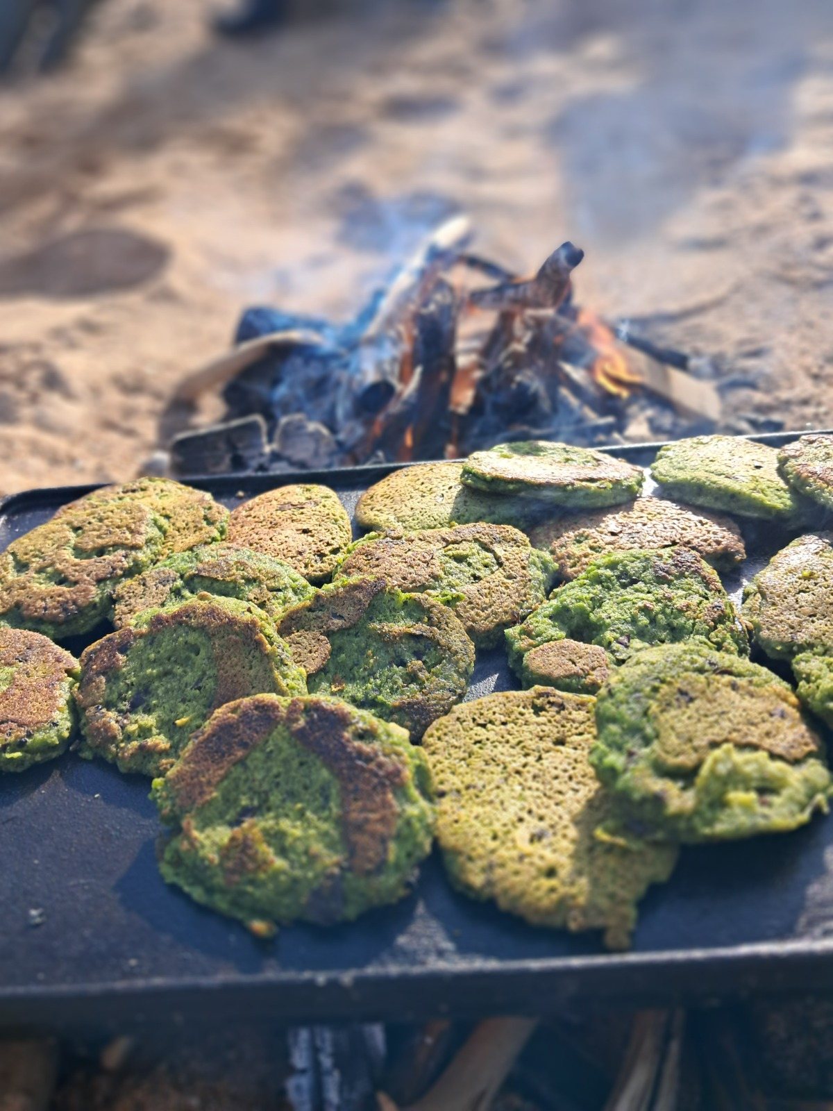 Green seaweed fritters cooking on a griddle over the fire