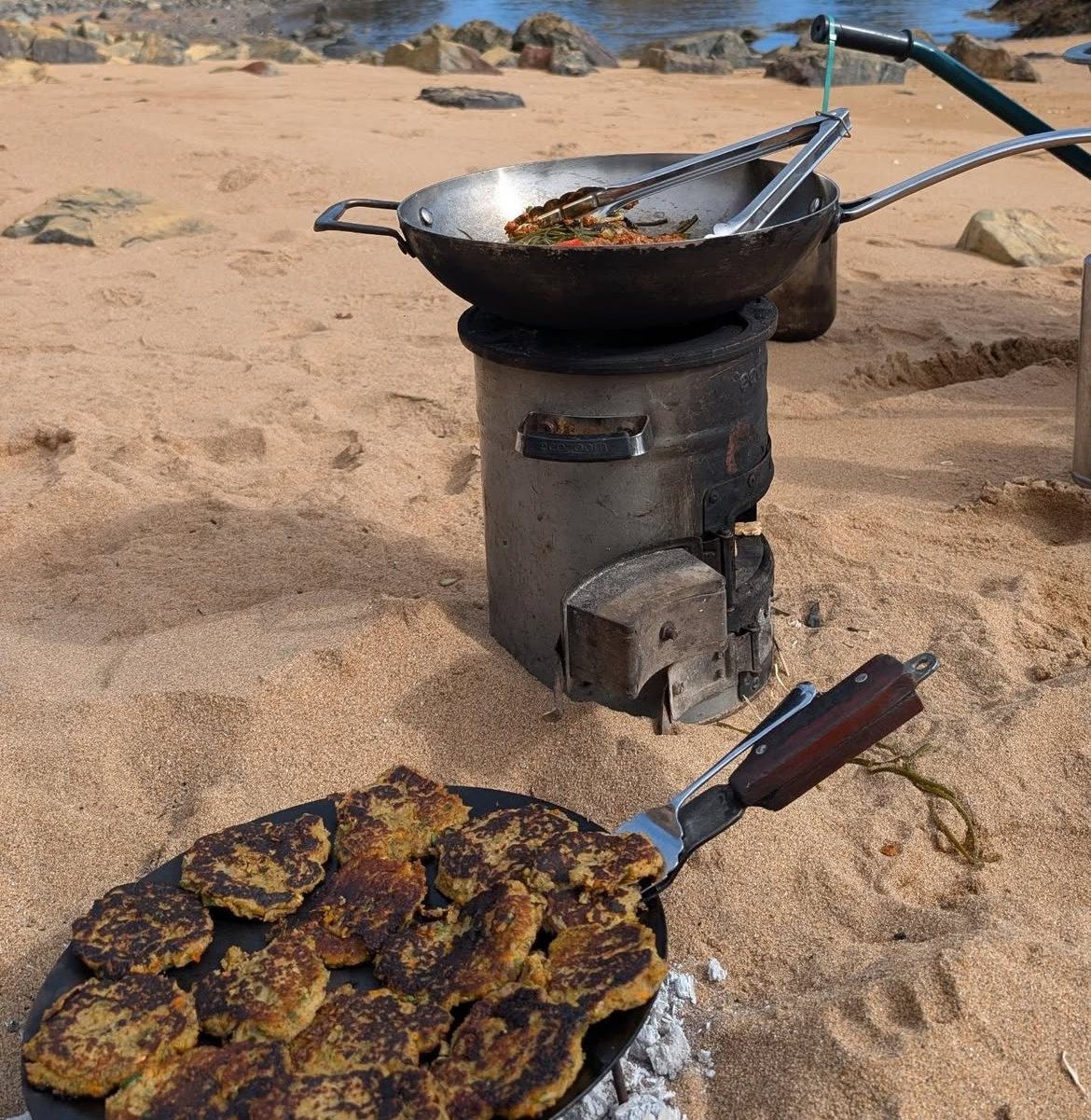 Mussel fritters cooking on a small stove on the sand