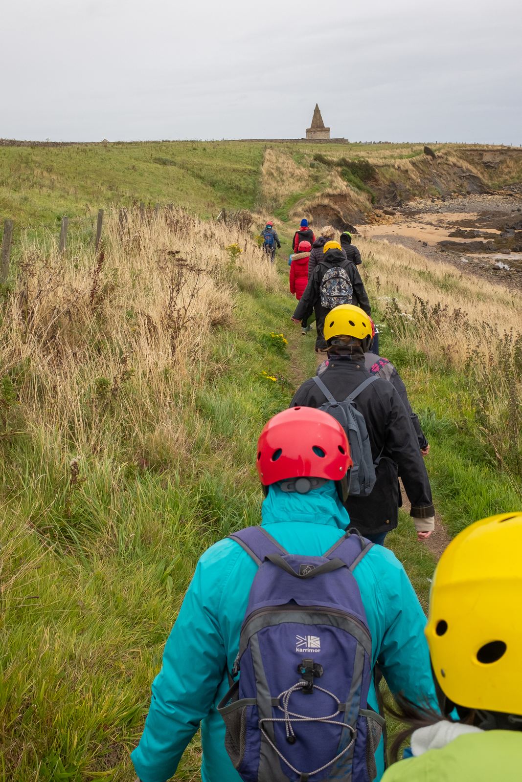 A workshop group in bright hi-visibility helmets walking the coast path to the shore