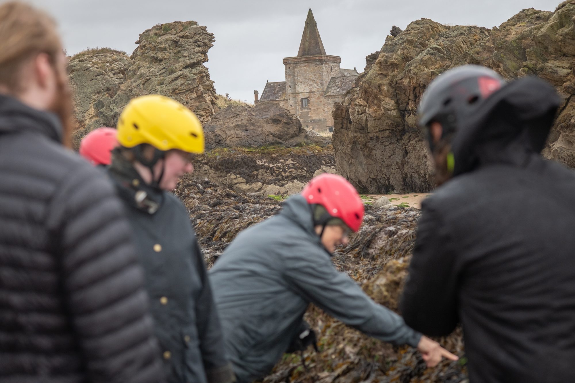 A helmeted workshop group foraging among the rocks below the Auld Kirk at St Monans
