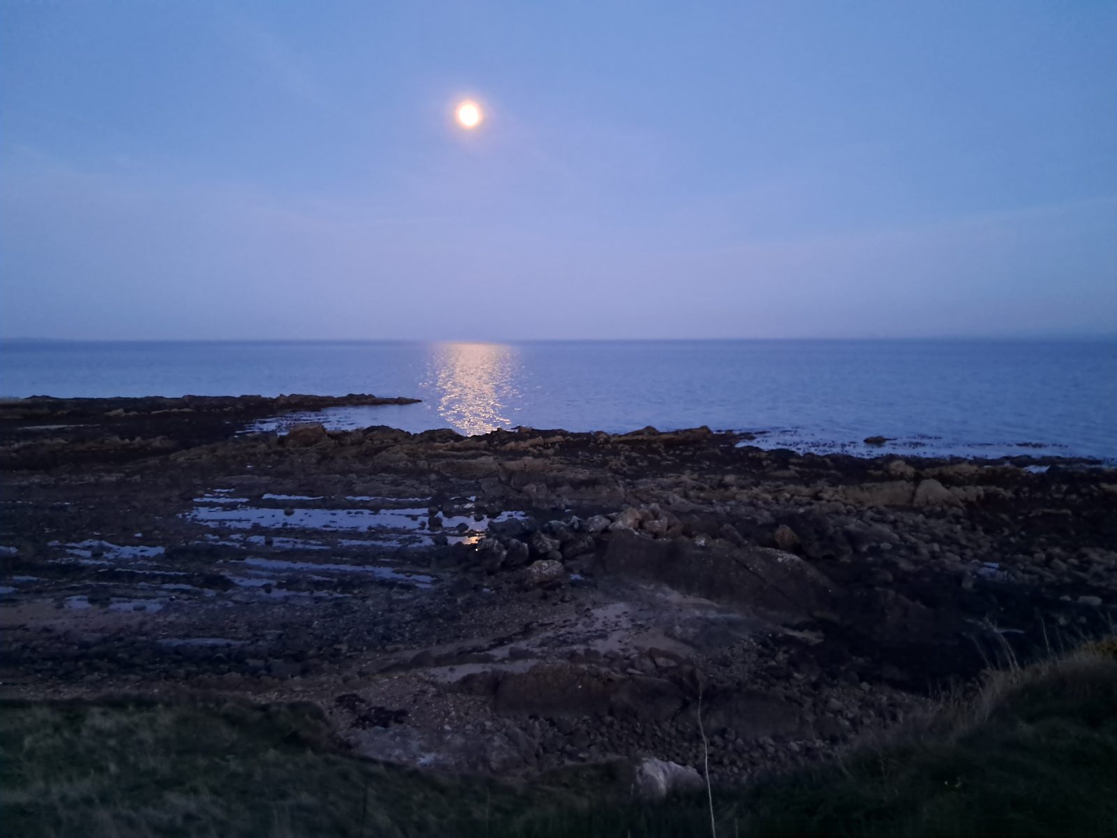 The moon rising over the sea and rocky shore at dusk