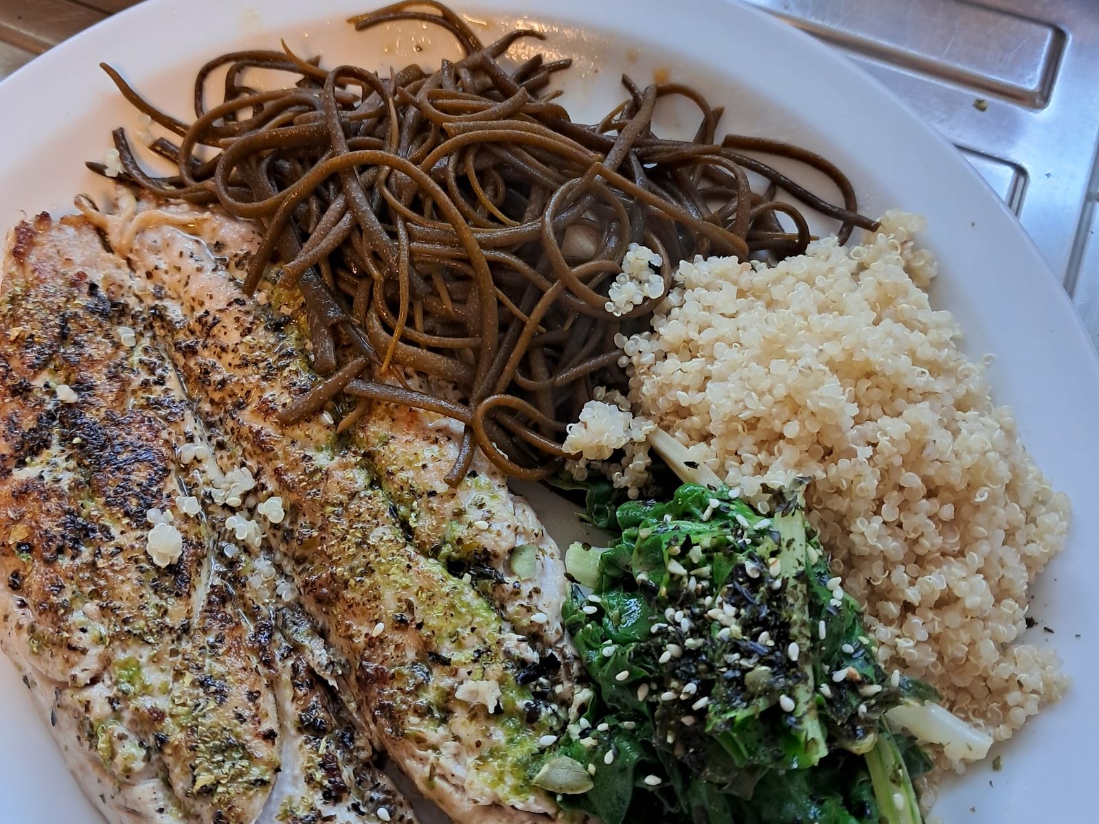 A plate of sea spaghetti, seaweed-crusted fish, grains and dressed greens