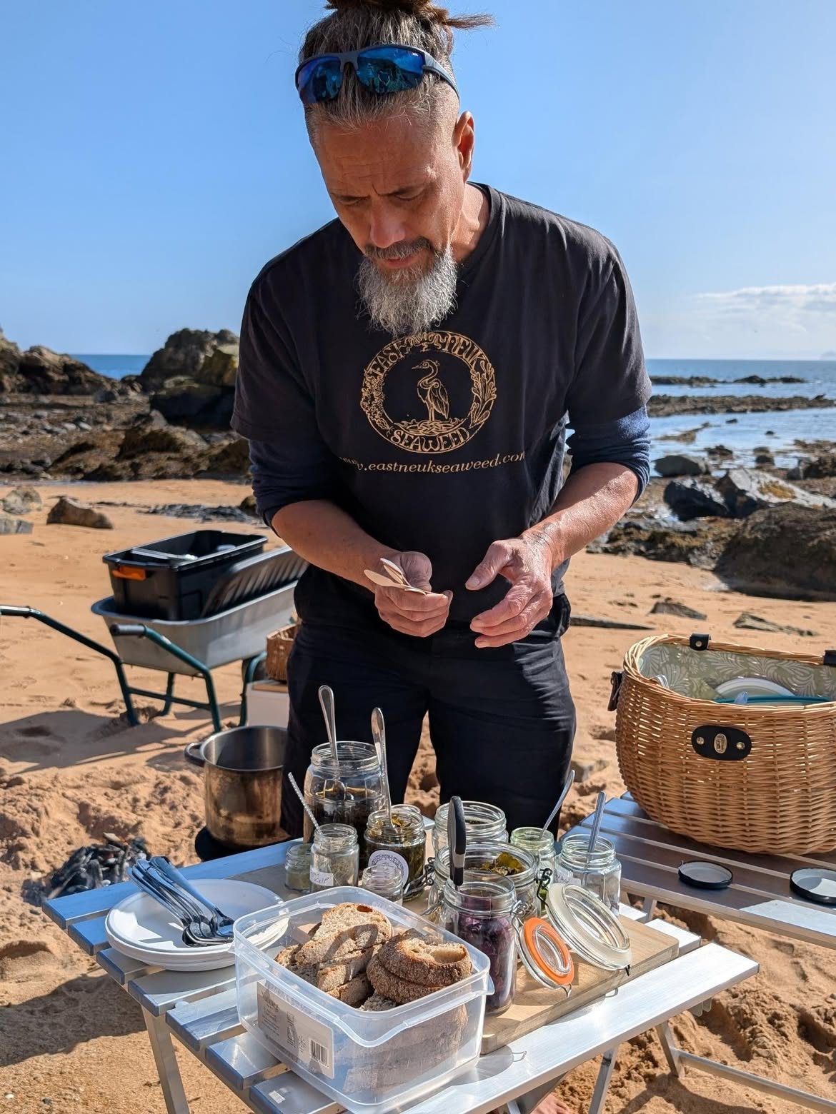 Jayson at a table of jars and baskets set up on the beach