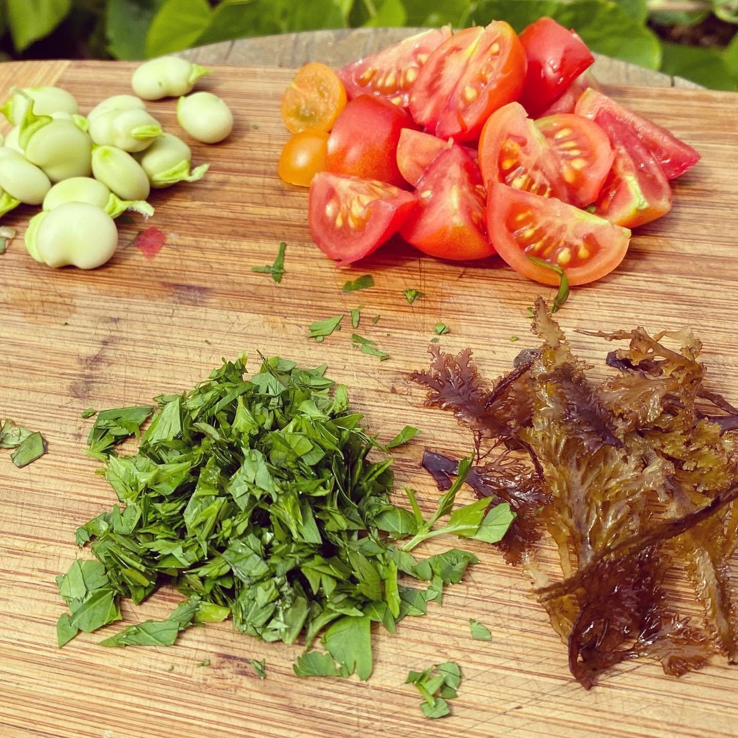 Broad beans, tomatoes, chopped herbs and dulse on a chopping board